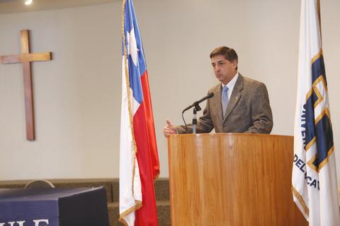 Un hombre habla desde un podio mientras se observan banderas chilena y de la universidad en el fondo.