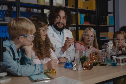 Un grupo de niños observa a un adulto que realiza un experimento científico en un laboratorio.