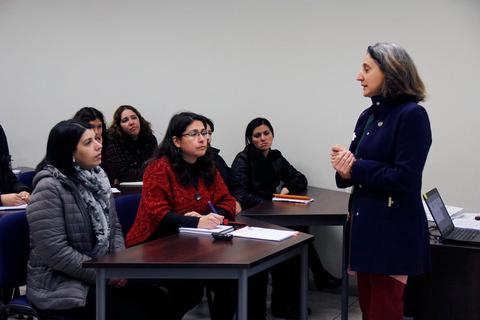 Una mujer está dando una charla frente a un grupo de mujeres que la escuchan atentamente en un aula.