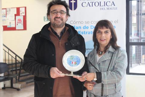 Dos personas sosteniendo un trofeo en un entorno académico.