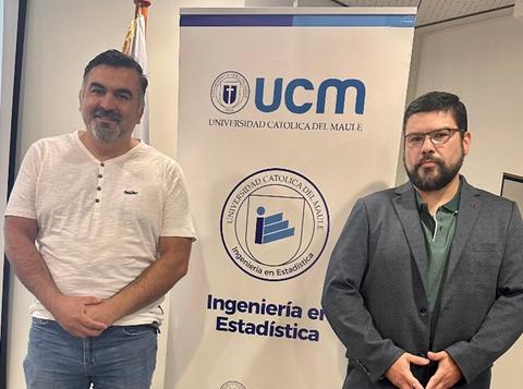 Dos hombres posan frente a una pancarta de la Universidad Católica del Maule.