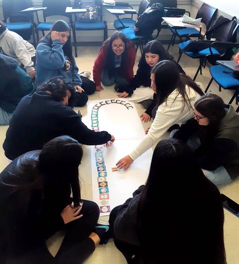 Un grupo de estudiantes se encuentra reunido en el suelo, trabajando en una actividad colaborativa con tarjetas y un papel grande.
