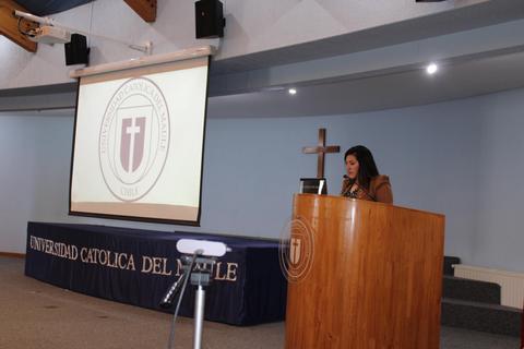 Una mujer presenta en un auditorio de la Universidad Católica del Maule con una proyección de fondo.