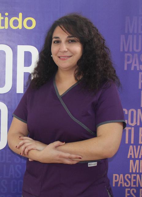Una mujer sonriente con cabello rizado vestido con una camiseta morada, de pie con los brazos cruzados.