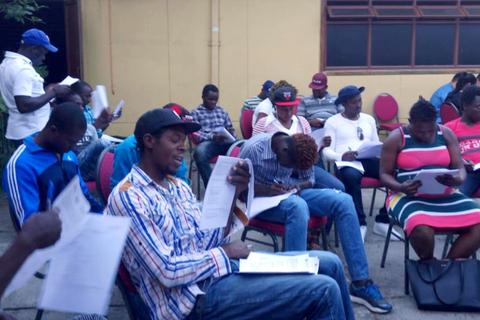 Un grupo de personas sentadas en sillas, revisando documentos en un espacio al aire libre.