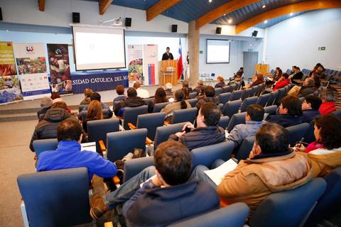 Una conferencia en la Universidad Católica del Maule con un auditorio lleno de asistentes.