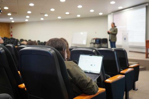 Una persona está atendiendo a una charla mientras usa su computador portátil en un auditorio.