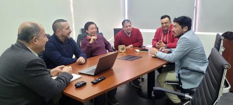 Un grupo de seis personas se reúne en una mesa de trabajo con una computadora portátil.