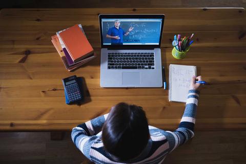 Una persona está tomando una clase en línea frente a una computadora portátil en una mesa de estudio.