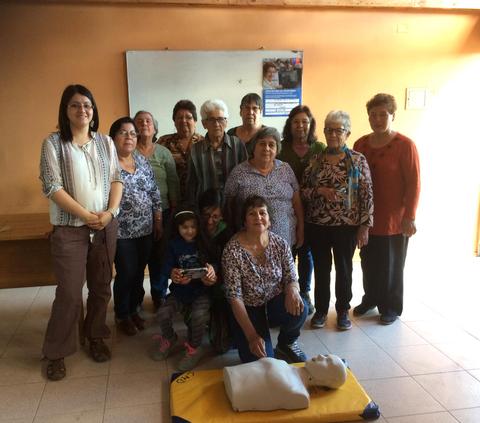 Un grupo de personas de diversas edades posando en una sala con un maniquí de simulación de primeros auxilios en el suelo.