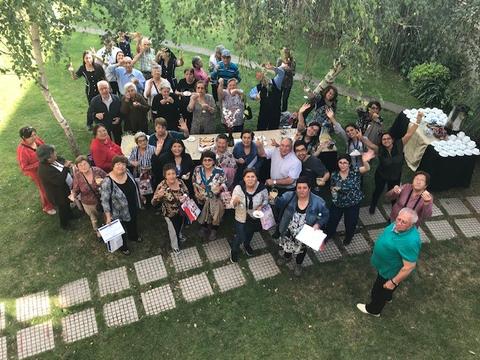 Un grupo grande de personas sonrientes y levantando la mano en un evento al aire libre.