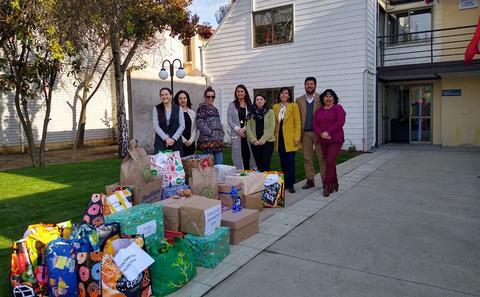 Grupo de personas posando frente a un edificio con varias cajas y bolsas de regalos en el suelo.