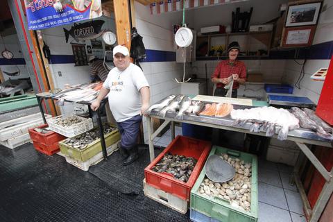 Dos vendedores en un mercado de pescado exhiben su mercancía en mesas de trabajo.