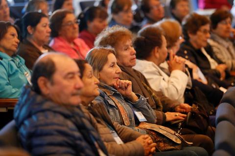 Grupo de personas mayores escuchando atentamente en un evento.