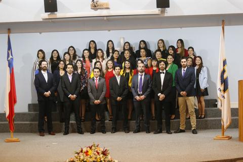 Un grupo de personas posando en un evento formal con banderas de Chile en el fondo.