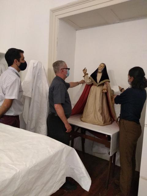 Tres personas observan cuidadosamente una figura religiosa en una mesa.