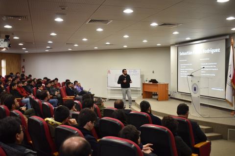 Un ponente presenta un tema a una audiencia en un auditorio.