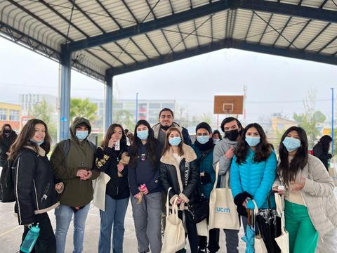 Un grupo de jóvenes sonríe en un espacio al aire libre bajo un toldo, todos llevan mascarillas.