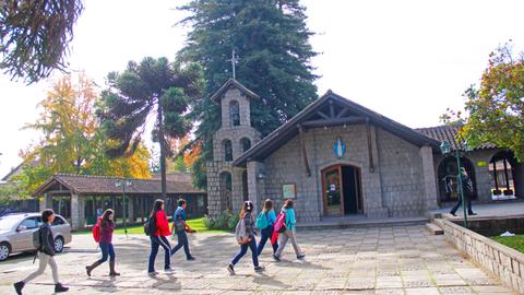 Un grupo de personas camina frente a una iglesia de estilo rústico en un entorno natural.