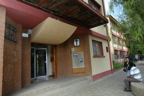 La imagen muestra la entrada de un edificio con una fachada moderna y un ambiente verde cercano.