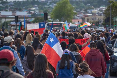 Una multitud de personas marcha sosteniendo banderas chilenas y otros símbolos en un ambiente de protesta.