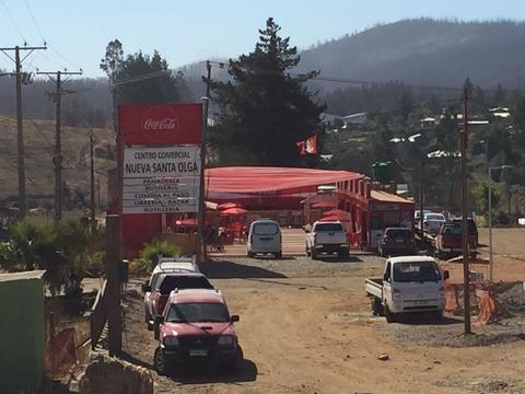 Una vista del centro comercial Nueva Santa Olga, con varios vehículos estacionados y un entorno rural.