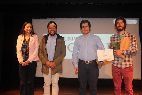 Un grupo de cuatro personas posando en un evento formal con un diploma en manos de uno de ellos.