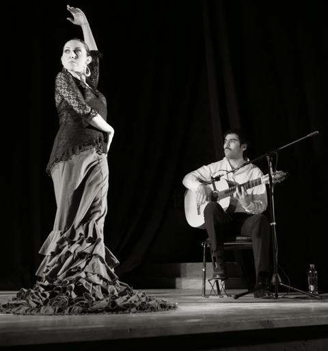 Una bailaora de flamenco se presenta en el escenario mientras un guitarrista la acompaña.