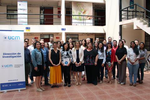Un grupo de personas posando en un espacio interior, junto a un cartel de la Dirección de Investigación de la UCM.