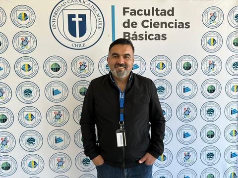 Una persona sonriente de pie frente a un fondo con logos de la Universidad Católica del Maule.