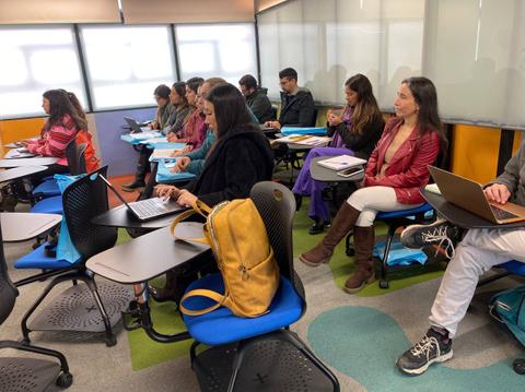 Un grupo de personas sentadas en un aula moderna, algunas trabajando en computadoras portátiles.