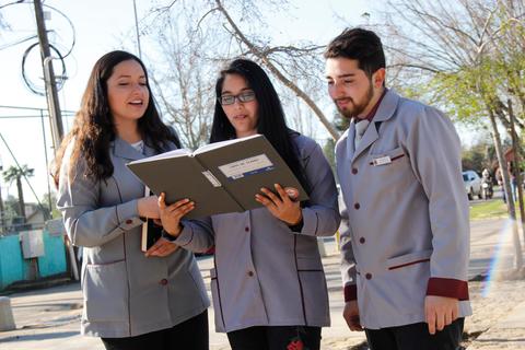 Tres estudiantes revisan un libro en un entorno al aire libre.