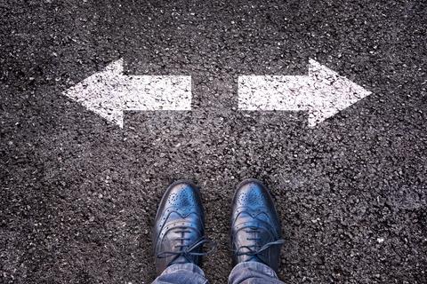 Un par de zapatos elegantes se encuentra en una encrucijada con flechas que indican dos direcciones distintas.