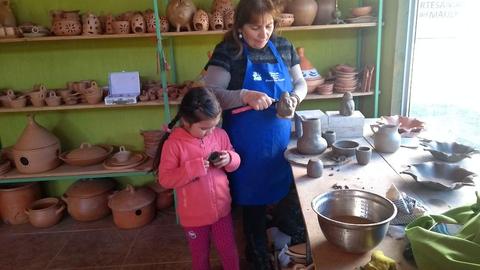 Una mujer y una niña están creando cerámica en un taller lleno de piezas de barro.