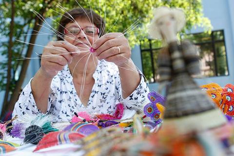 Una mujer trabaja en la creación de artesanías con hilos coloridos y se enfoca en una pieza con delicadeza.