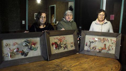 Tres mujeres están mostrando cuadros decorativos con elementos artísticos en un entorno interior.