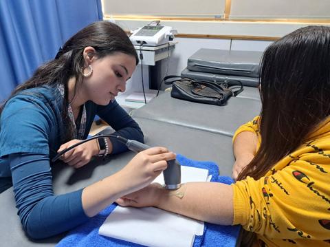 Una joven está aplicando un diseño en la piel de otra persona en un entorno de consulta.