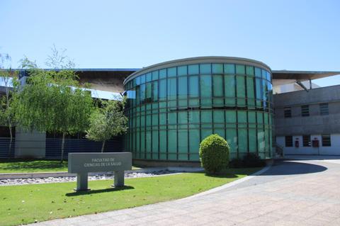 Edificio moderno de la Facultad de Ciencias de la Salud con un diseño de vidrio y vegetación alrededor.