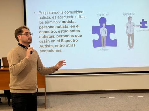 Un hombre está presentando en un aula, hablando sobre términos adecuados para referirse a la comunidad autista.