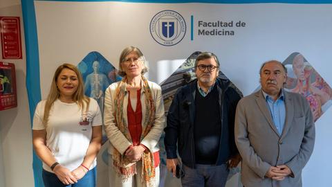 Cuatro personas posan frente a un fondo que representa la Facultad de Medicina.