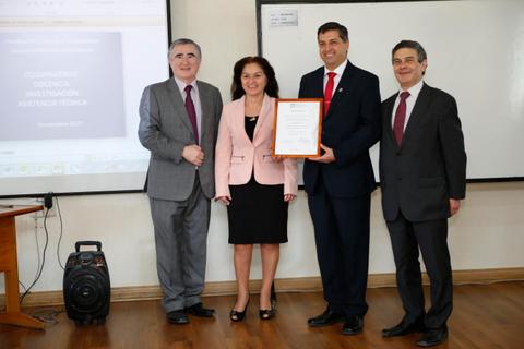 Cuatro personas posan junto a un certificado en un entorno académico.