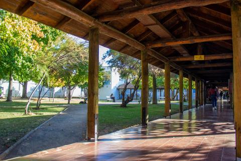 Imagen de un pasillo techado con columnas de madera que da a un jardín con árboles.