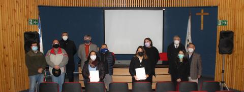 Grupo de personas en un evento formal en un salón con proyector y banderas.