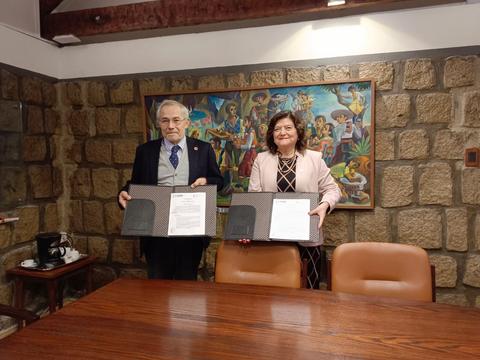 Dos personas sosteniendo documentos frente a una pintura colorida en una sala de reuniones.