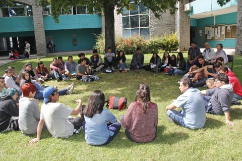 Un grupo de jóvenes sentados en círculo en un espacio verde, participando en una actividad grupal.
