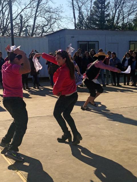 Un grupo de personas participa en una actuación de baile al aire libre, con una audiencia mirando desde el fondo.