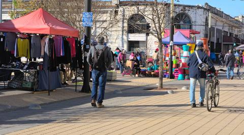 Una escena de un mercado al aire libre con puestos de ropa y varios visitantes.
