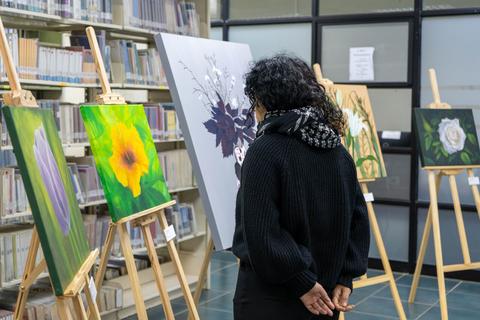 Una persona observa obras de arte en una exposición dentro de una biblioteca.