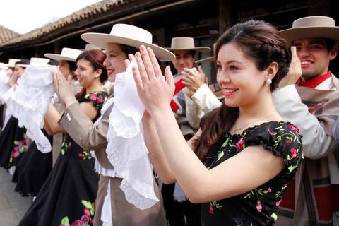 Un grupo de personas vestidas con trajes tradicionales están realizando una danza folclórica mientras aplauden con pañuelos en las manos.