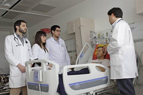 Un grupo de profesionales de la salud se encuentra en una sala de hospital hablando con un paciente en cama.